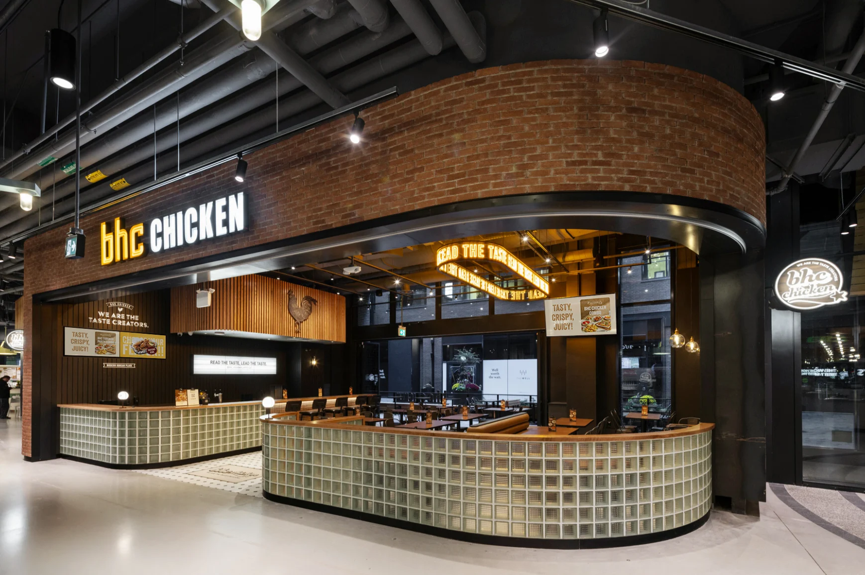 A BHC Chicken storefront: a brick-fronted counter with glass-block detailing and dining area, under illuminated bhc CHICKEN signage