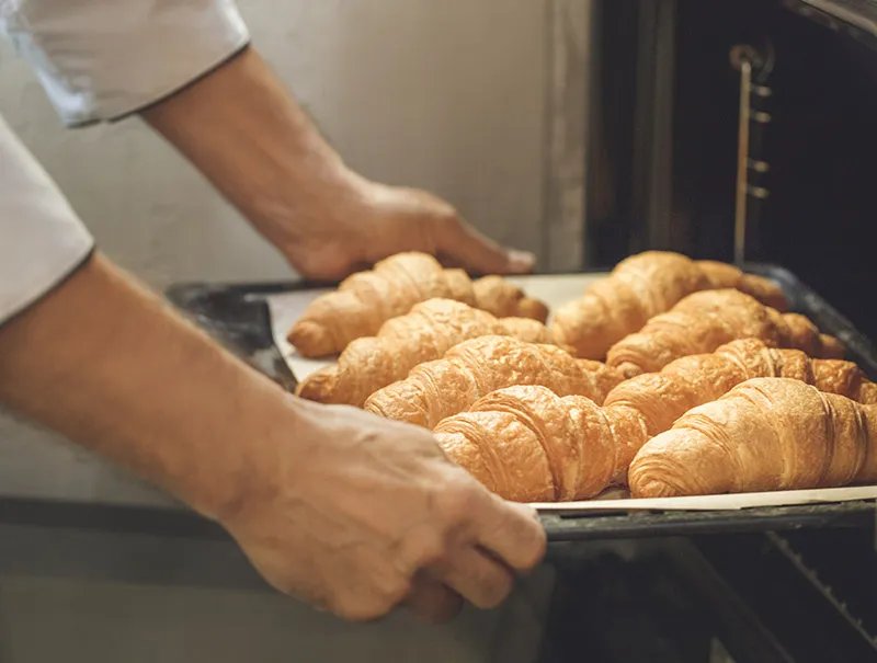 A baker pulling a tray of freshly baked croissants out of the oven